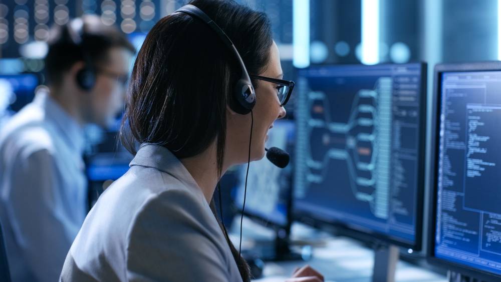 In the System Control Room Technical Operator Sits and Monitors Various Activities Showing on Multiple Displays with Graphics.
